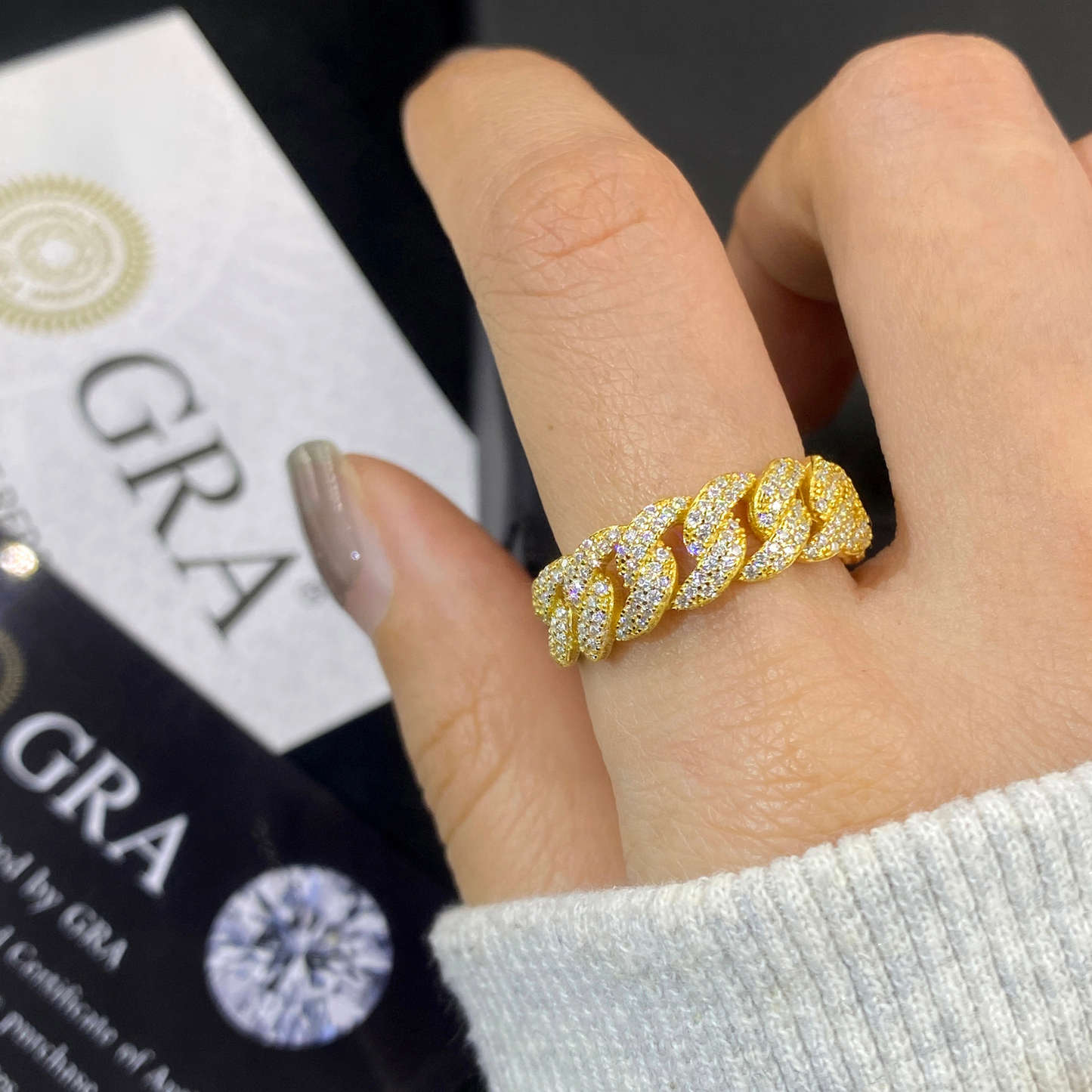 Gold ring with diamonds on a finger, with 'GRA' branding in the background