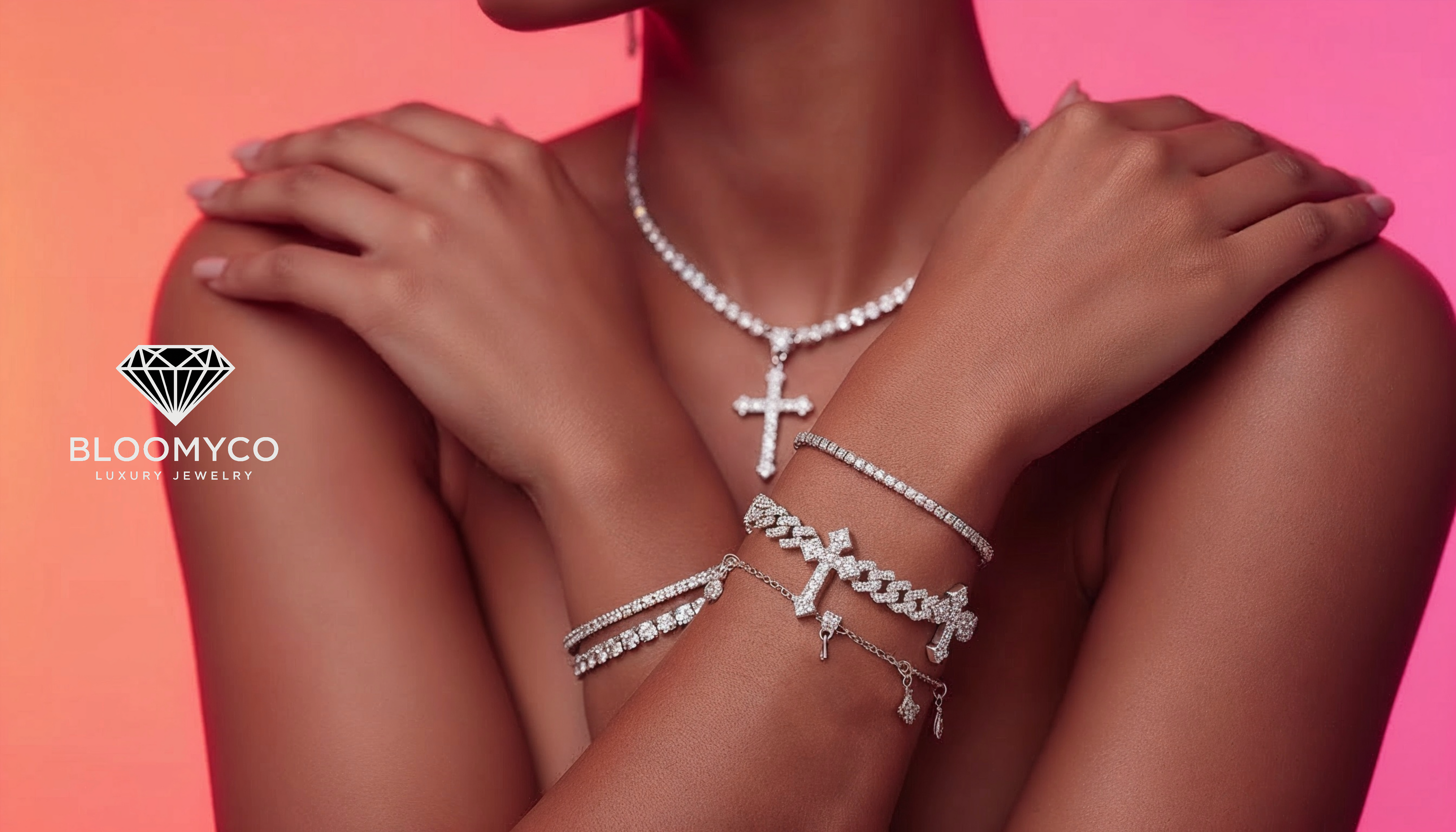 Silver jewelry including a necklace, bracelet, and cross pendant on a person against a pink background with Bloomyco logo.