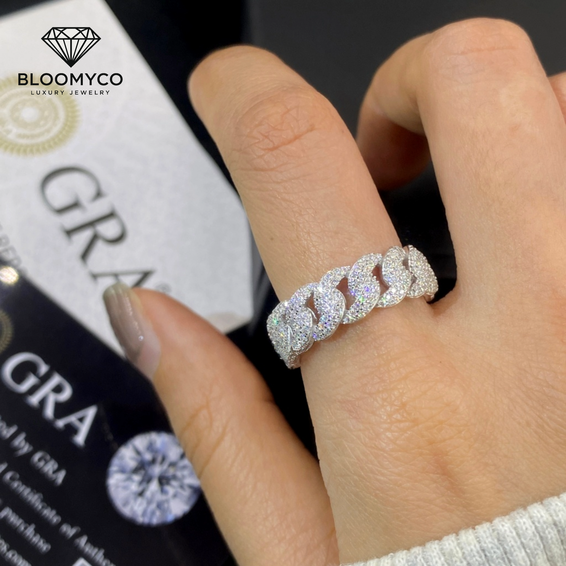 Diamond ring on a finger with Bloomyco branding in the background